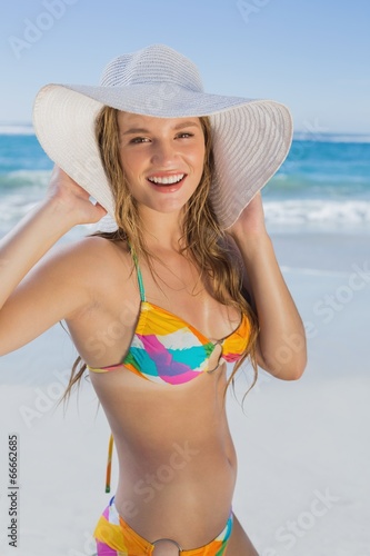 Beautiful girl in bikini and straw hat on the beach smiling at c