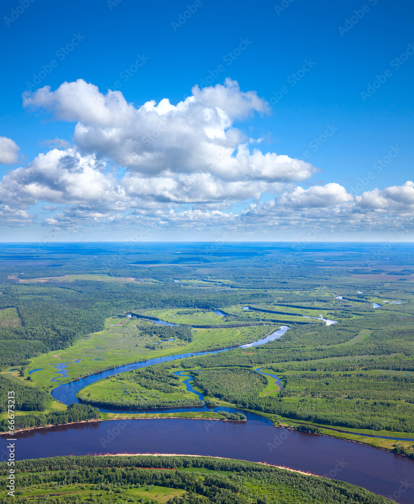 Forest river under white clouds, top view