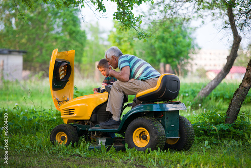 Grandfather and grandson at sunset checking lawn mower