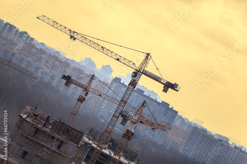 Construction cranes over buildings against yellow sky