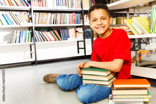 Smiling schoolchild with pile of books on floor