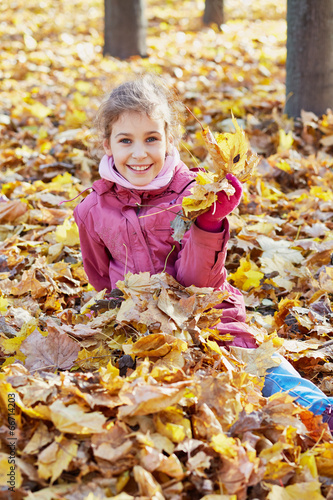 little girl in red jacket sits in drift of maple fallen leafes