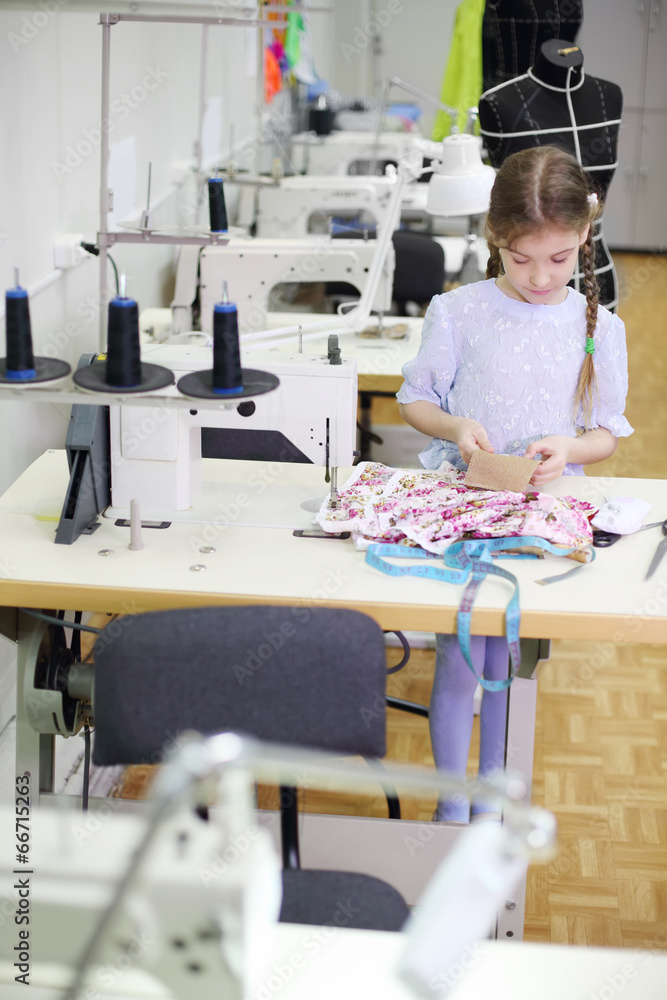 Girl stands near table with sewing machine and holds cloth Girl stands near table with sewing machine and holds cloth