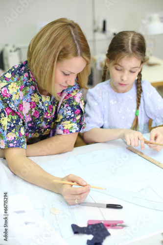 Smiling female tailor and student girl draw patterns for clothes