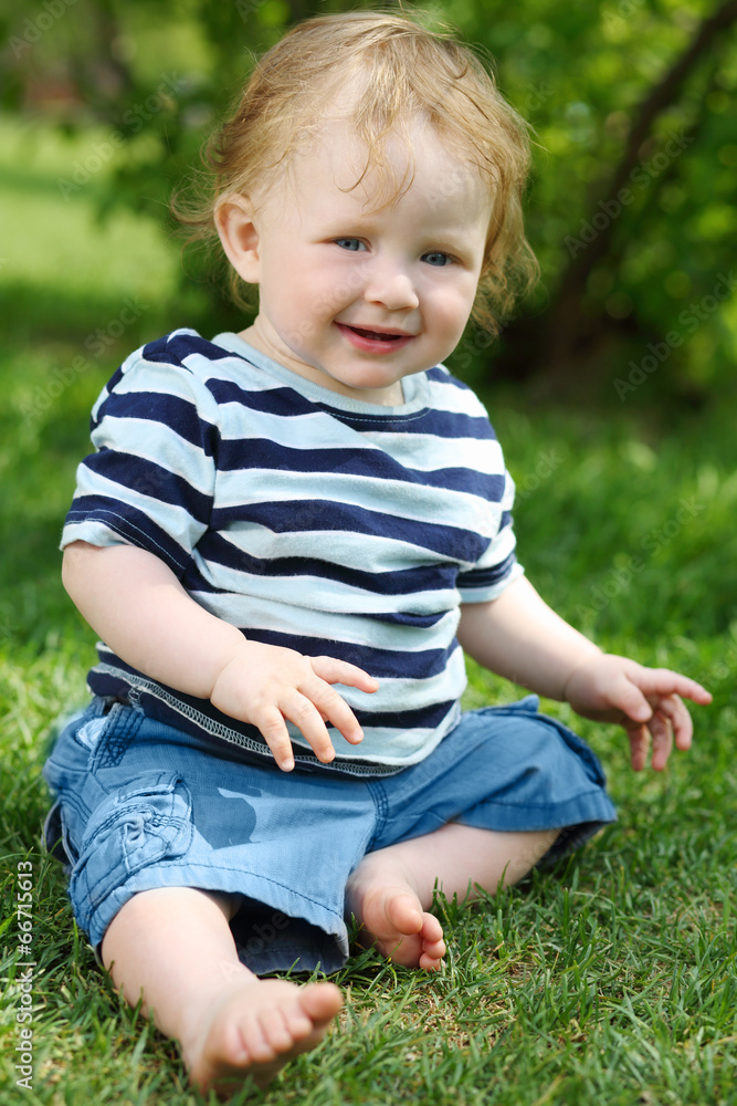 Little barefoot boy in shorts sitting on green grass Little barefoot boy in shorts sitting on green grass