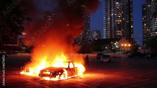 Two cars burn in parking lot with highrise at dusk photo