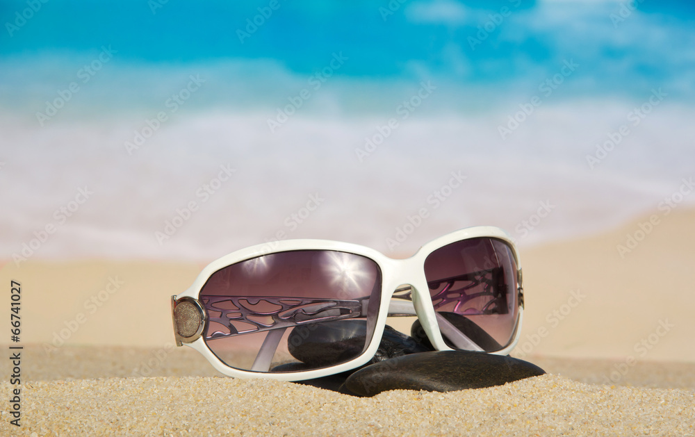 Sunglasses and pebbles on sand