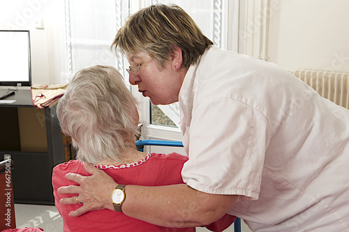 Cheerful care giver helping elderly woman at home, embracing her
