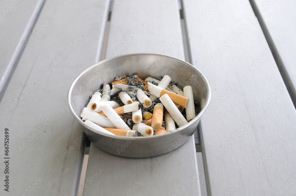 Many used cigarettes in aluminium ashtray on wooden table Many used cigarettes in aluminium ashtray on wooden table