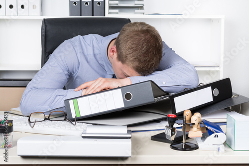Junger erschöpfter Mann liegt auf Schreibtisch im Büro