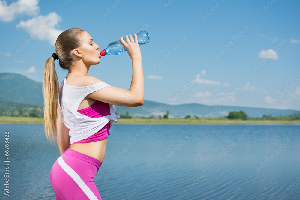 Young fitness woman drinking water after workout by the sea