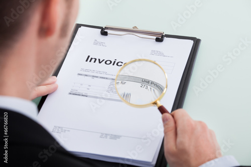 Businessman Examining Invoice Through Magnifying Glass