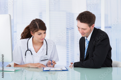 Doctor Showing Report To Businessman In Clinic