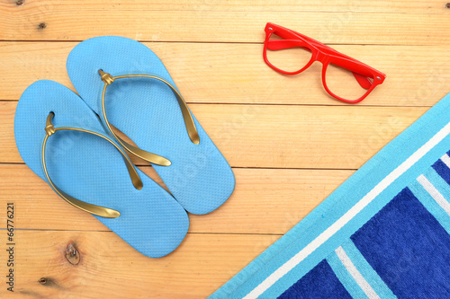 Beach slippers, towel and sunglasses on wood