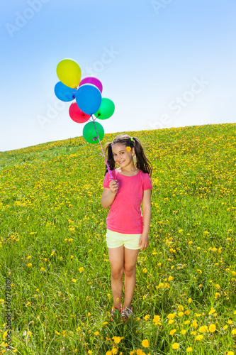 Cute girl with flying balloons stands on grass