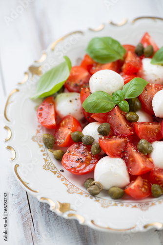 Caprese salad with capers on a plate, vertical shot, close-up
