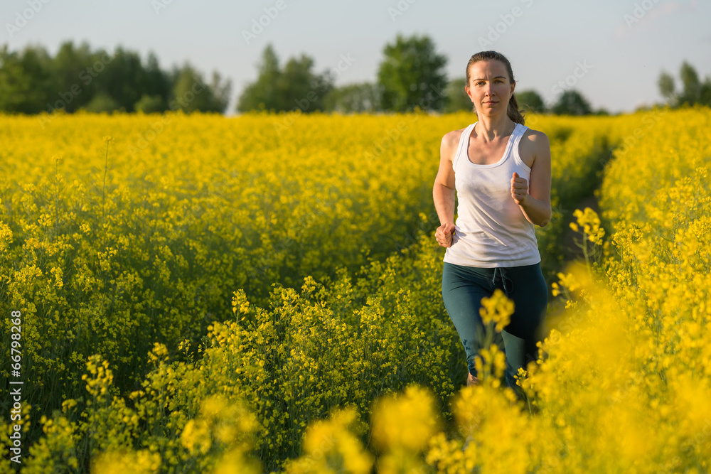 Young woman is jogging in yellow rapeseed field at sunset Young woman is jogging in yellow rapeseed field at sunset