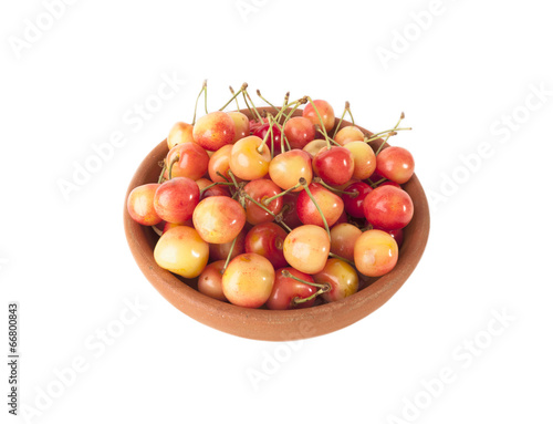 Red and yellow cherries in clay bowl on white