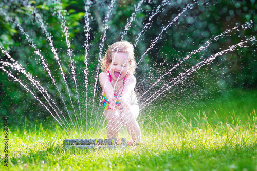 Happy girl playing with garden sprinkler photo