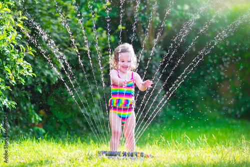 Sweet girl playing with garden sprinkler photo