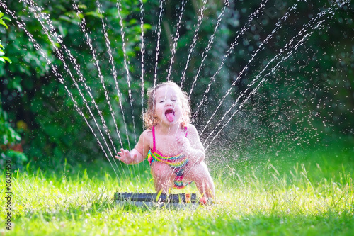 Funny girl playing with garden sprinkler photo