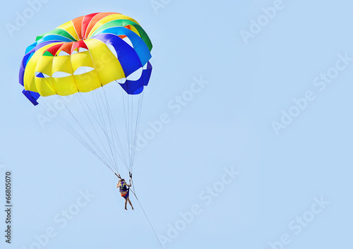 Девушка летит в голубом небе на красочном, разноцветном парашюте