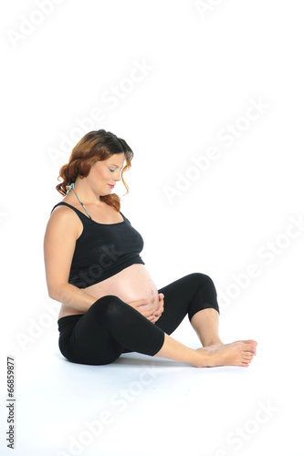 Schwangere Frau sitzt im Schneidersitz am Boden und streichelt ihren schwangeren Bauch 
