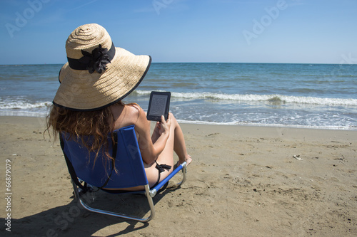 a girl reading ebook on a chair on the beach