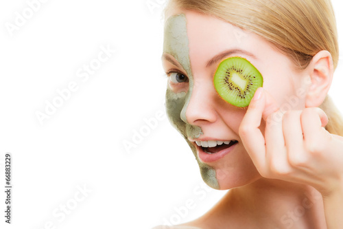 Woman in clay mask on face covering eye with kiwi photo