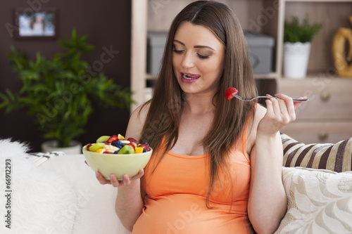 Pregnant woman eating fruit salad at home