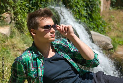 Guy in sunglasses resting in nature near the waterfall