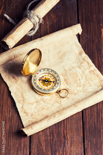 old unrolled map, rolled map and compass on wooden table