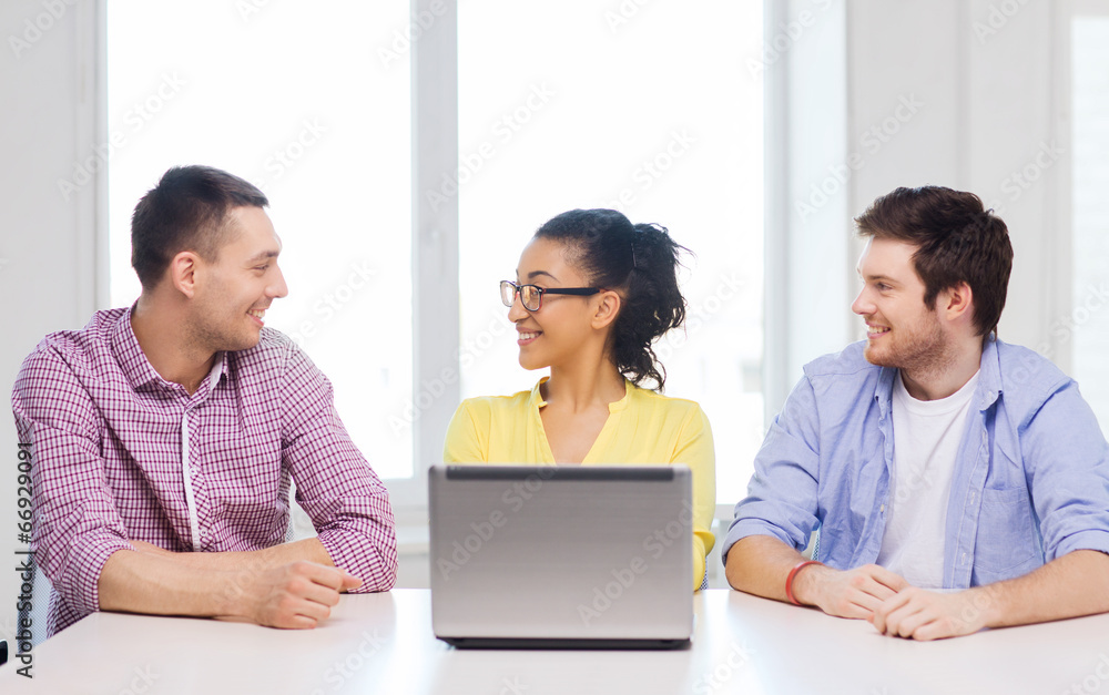 three smiling colleagues with laptop in office three smiling colleagues with laptop in office
