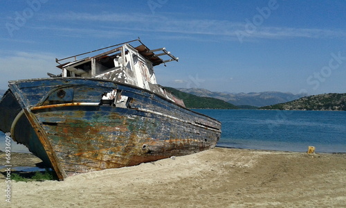 shipwrecked boat beached on sand with sea and mountains photo