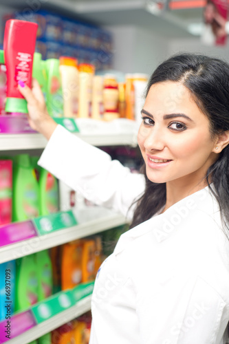 young woman holding bottle of shampoo in supermarket