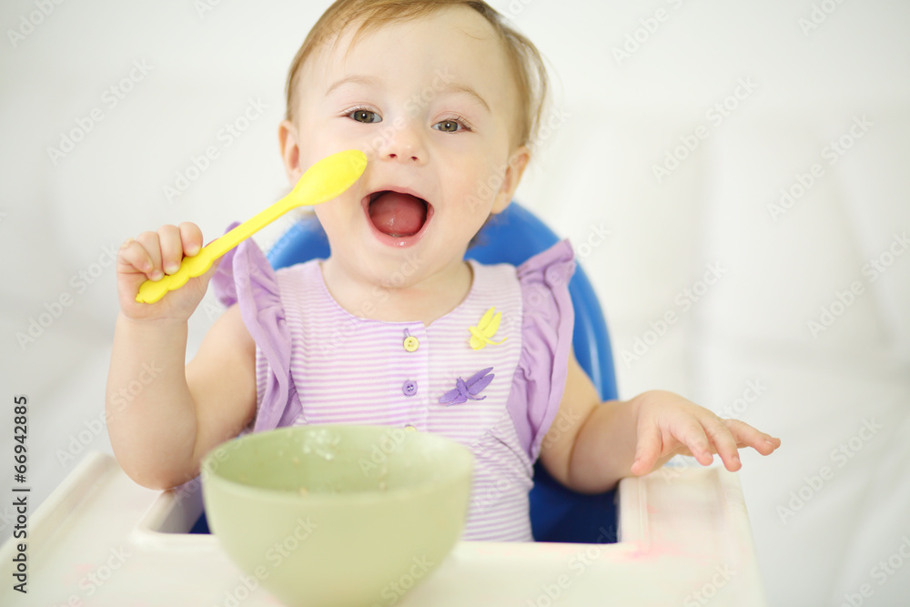 Little happy baby with spoon sits at highchair and eats porridge Little happy baby with spoon sits at highchair and eats porridge