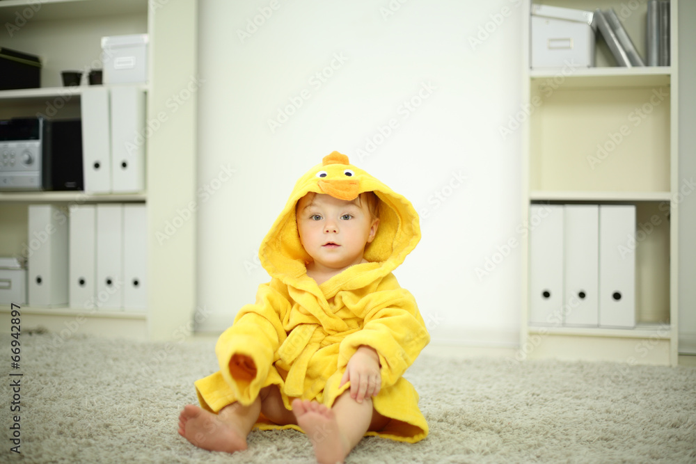 Little cute baby in yellow robe sits on white carpet in room Little cute baby in yellow robe sits on white carpet in room