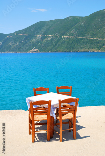 Dining table with chairs in a greek taverna with blue sea and gr