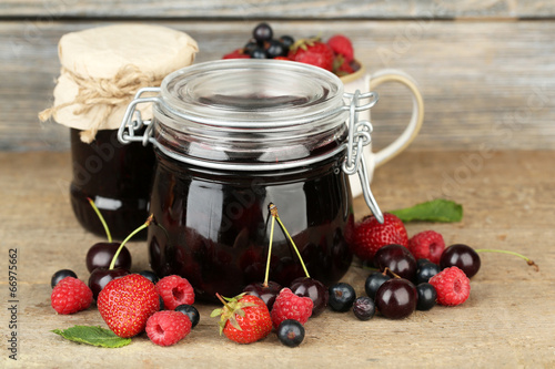 Tasty jam with berries in glass jars on wooden table