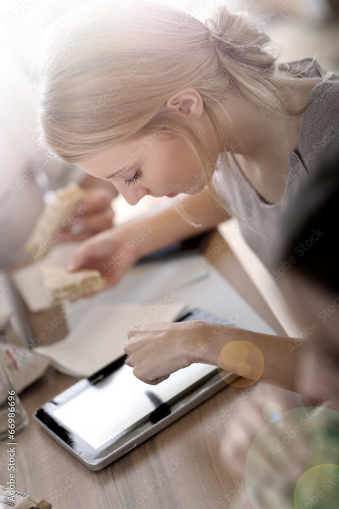 Young woman at work eating sandwich and using tablet Young woman at work eating sandwich and using tablet