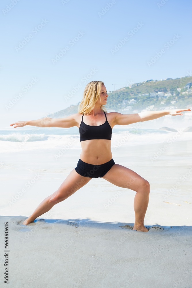 Fit blonde in warrior pose on the beach