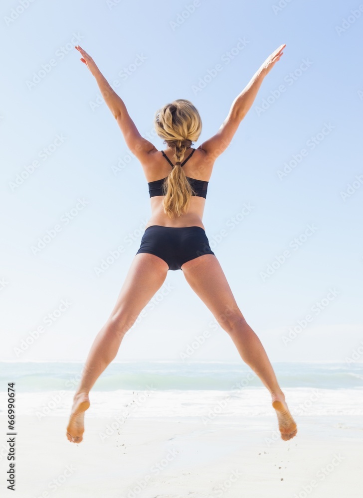 Fit blonde jumping on the beach with arms outstretched