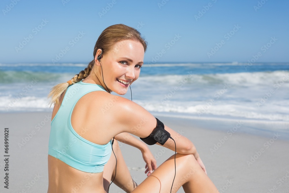 Fit woman sitting on the beach taking a break smiling at camera Fit woman sitting on the beach taking a break smiling at camera