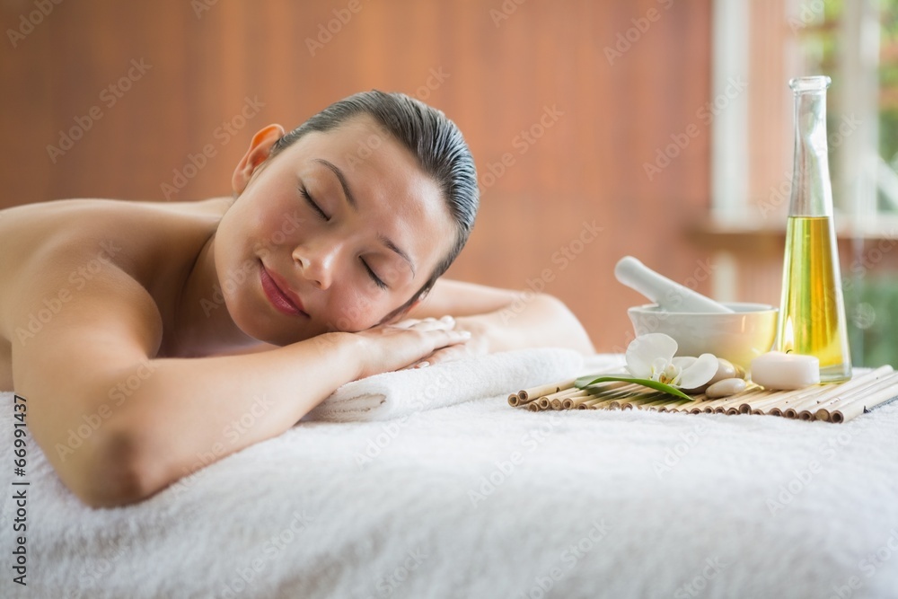Brunette lying on massage table with tray of beauty treatments - obrazy, fototapety, plakaty 