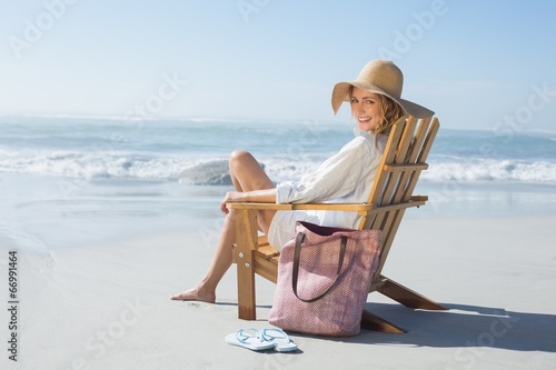 Canvastavla Smiling blonde sitting on wooden deck chair by the sea