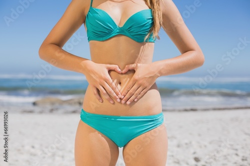 Fit woman in bikini on the beach making heart shape on stomach