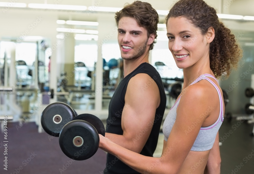 Fit couple lifting dumbbells together smiling at camera Fit couple lifting dumbbells together smiling at camera