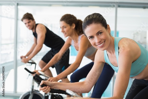 Fit people in a spin class with brunette smiling at camera