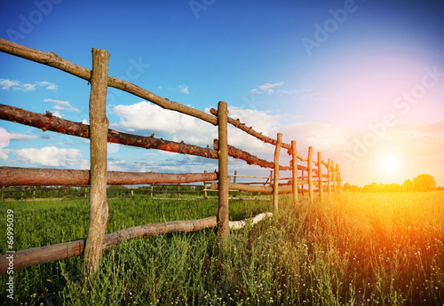 Fence in the green field under blue cloud sky