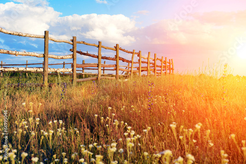 Fence in the green field under blue cloud sky